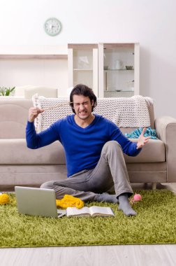 Genç yakışıklı adam evde örgü örüyor.