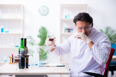 Erkek kimyager laboratuvarda şarap örneklerini inceliyor.