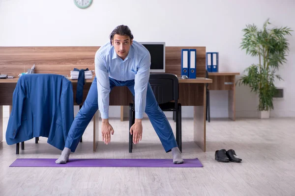 Jonge knappe zakenman doet oefeningen op het werk — Stockfoto