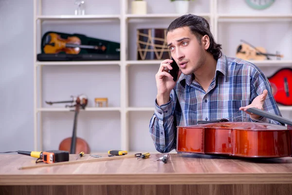 Mladý pohledný opravář opravuje violoncello — Stock fotografie