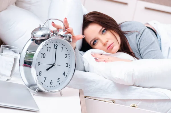 Ung kvinna ligger på sängen i tid management koncept — Stockfoto