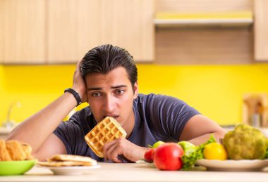 Sağlıklı ve sağlıksız yemek arasında zor bir seçim yapan bir adam.