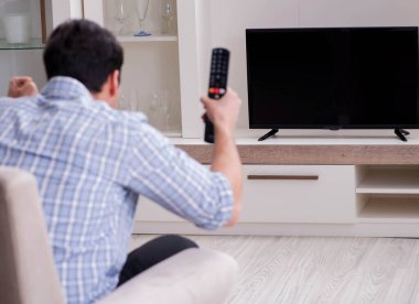 Genç adam evde televizyon izliyor.