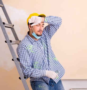 Genç müteahhit zımpara kağıdıyla duvarı zımparalıyor.