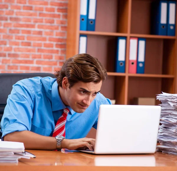 Jovem funcionário com excesso de trabalho sentado no escritório — Fotografia de Stock