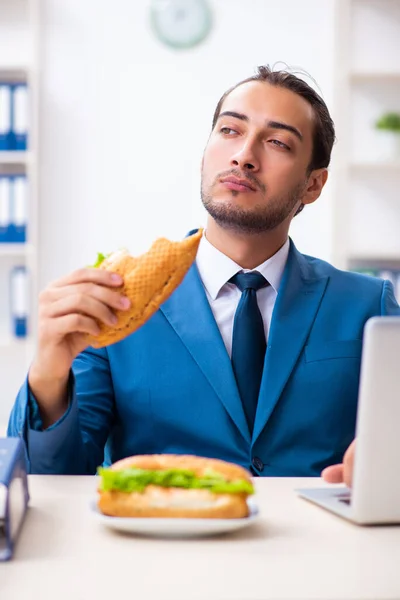 Ung manlig anställd som äter frukost på arbetsplatsen — Stockfoto