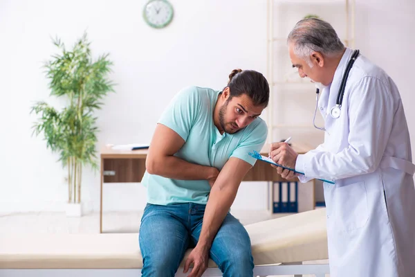 Gewonde jongeman op bezoek bij oude dokter — Stockfoto