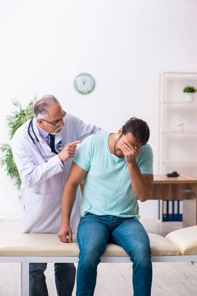 Gewonde jongeman op bezoek bij oude dokter — Stockfoto