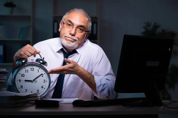 Oude mannelijke werknemer die laat op kantoor werkt — Stockfoto