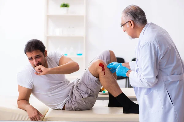 Leg rannego człowieka odwiedzając starego lekarza w koncepcji pierwszej pomocy — Zdjęcie stockowe