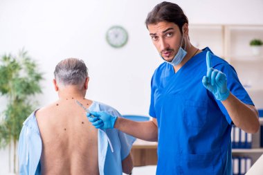 Yaşlı adam genç erkek doktor dermatoloğu ziyaret ediyor.