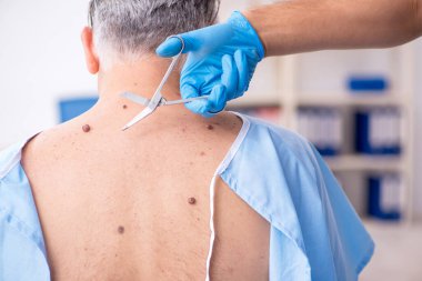 Yaşlı adam genç erkek doktor dermatoloğu ziyaret ediyor.