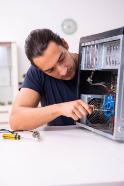 Genç adam evde bilgisayar tamir ediyor.