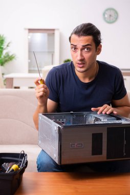 Genç adam evde bilgisayar tamir ediyor.