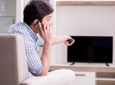 Genç adam evde televizyon izliyor.