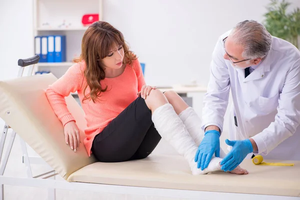 Joven pierna lesionada mujer visitando viejo médico traumatólogo —  Fotos de Stock