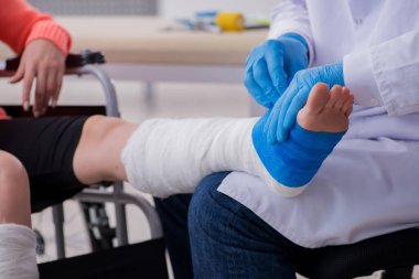 Genç bacak yaralı kadın yaşlı doktor travmatoloğu ziyaret ediyor.