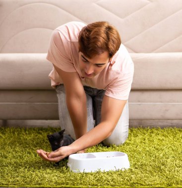 Genç adam evde kedi yavrusuyla oynuyor.