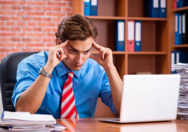 Ofiste aşırı işi olan genç bir çalışan oturuyor.