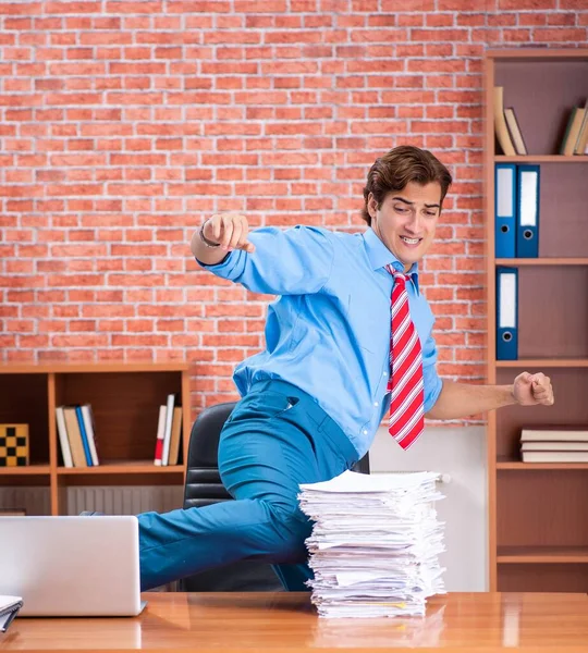Mladý zaměstnanec s nadměrnou prací sedí v kanceláři — Stock fotografie