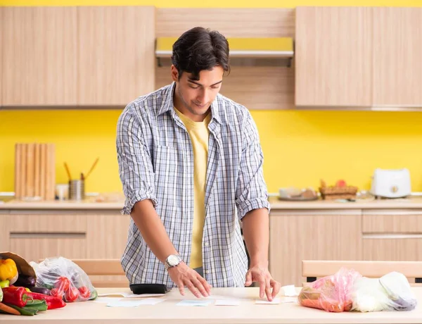 Joven calculando gastos para verduras en la cocina — Foto de Stock