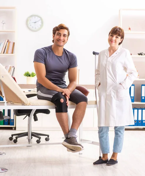 Bonito jogador de futebol americano visitando médico traumato feminino — Fotografia de Stock