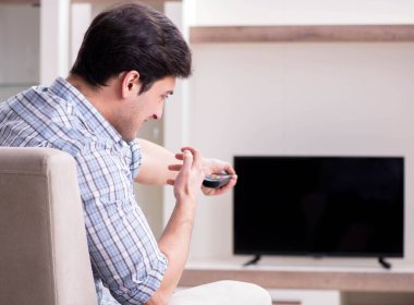 Genç adam evde televizyon izliyor.