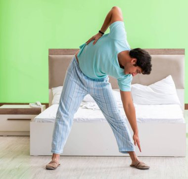 Pijamalı genç adam sabah egzersizi yapıyor.