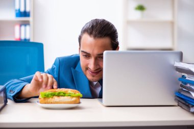 Genç erkek çalışan işyerinde kahvaltı yapıyor.