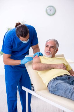 Yaralı yaşlı adam genç erkek doktor travmatoloğu ziyaret ediyor.