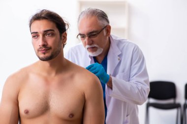 Yaralı genç adam deneyimli erkek doktoru ziyaret ediyor.