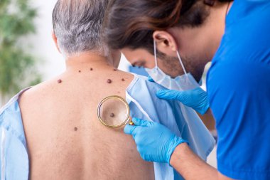Yaşlı adam genç erkek doktor dermatoloğu ziyaret ediyor.