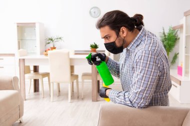 Genç erkek müteahhit Coronavirus konseptiyle evi temizliyor.