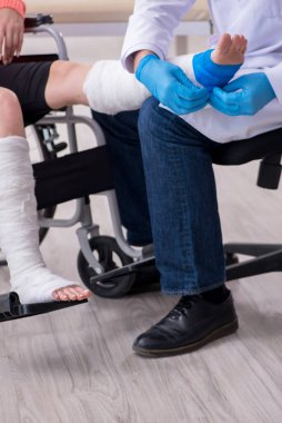 Genç bacak yaralı kadın yaşlı doktor travmatoloğu ziyaret ediyor.