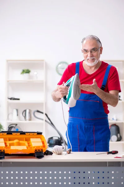 Old male contractor repairing iron indoors — Stock Photo, Image