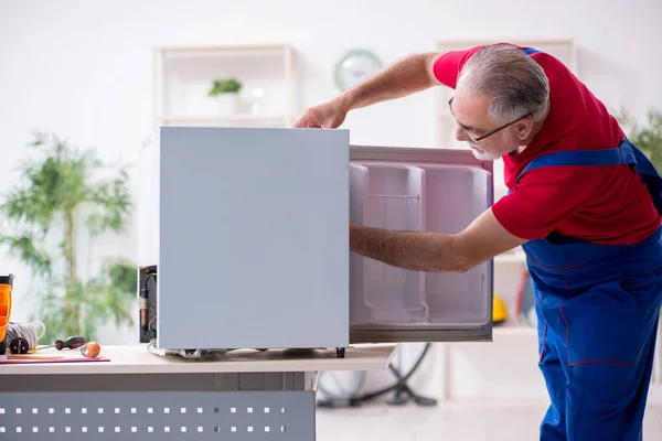 Старый подрядчик ремонтирует холодильник в помещении — стоковое фото