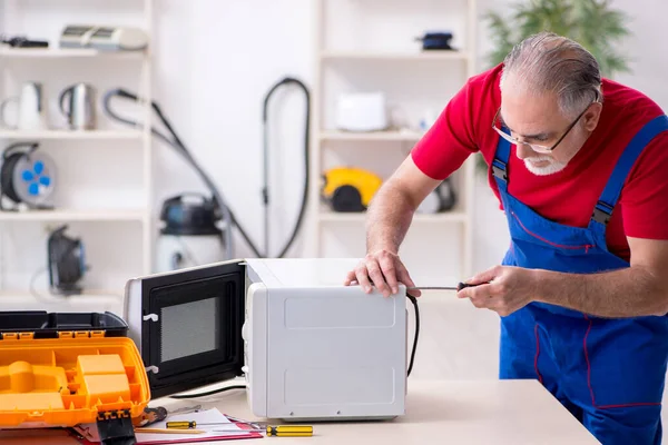 Empreiteiro velho do sexo masculino reparar microondas dentro de casa — Fotografia de Stock