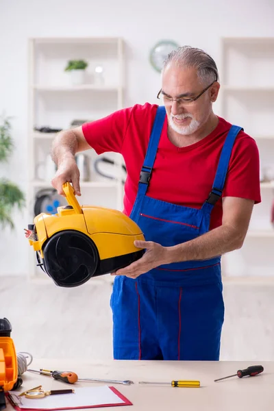 Evde elektrik süpürgesi tamir eden yaşlı bir erkek müteahhit. — Stok fotoğraf