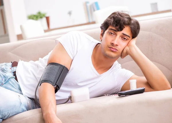 Homem jovem medindo a pressão arterial em casa — Fotografia de Stock
