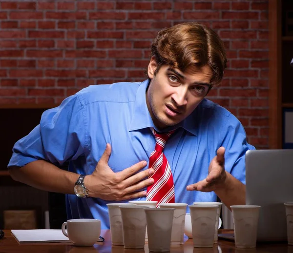 Jovem funcionário bebendo café trabalhando no turno da noite — Fotografia de Stock