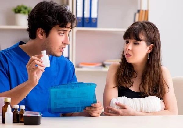 Young woman with bandaged arm visiting male doctor traumotologis — Stock Photo, Image