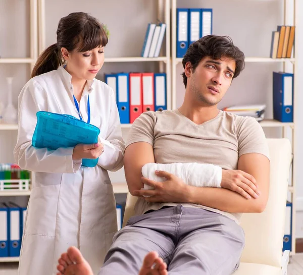 Ung man med bandagerad arm besöker kvinnlig läkare traumatologis — Stockfoto