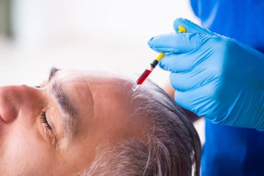 Yaşlı adam saç nakli için genç erkek doktoru ziyaret ediyor.