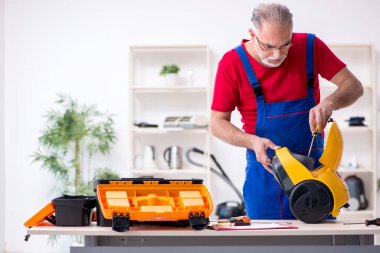 Evde elektrik süpürgesi tamir eden yaşlı bir erkek müteahhit.