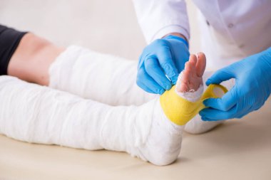 Genç bacak yaralı kadın yaşlı doktor travmatoloğu ziyaret ediyor.
