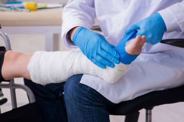 Genç bacak yaralı kadın yaşlı doktor travmatoloğu ziyaret ediyor.
