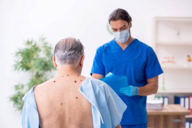 Yaşlı adam genç erkek doktor dermatoloğu ziyaret ediyor.