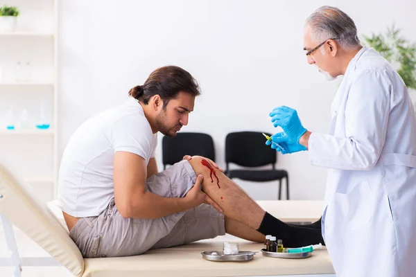 Нога поранений чоловік, який відвідує старого лікаря в концепції першої допомоги — стокове фото