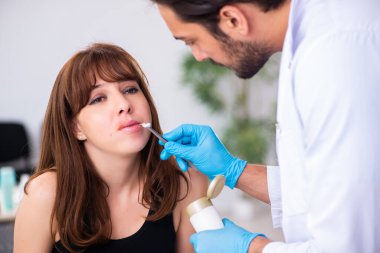 Genç bir kadın erkek doktor dermatoloğunu ziyaret ediyor.