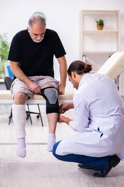 Viejo hombre herido visitando joven médico traumatólogo —  Fotos de Stock